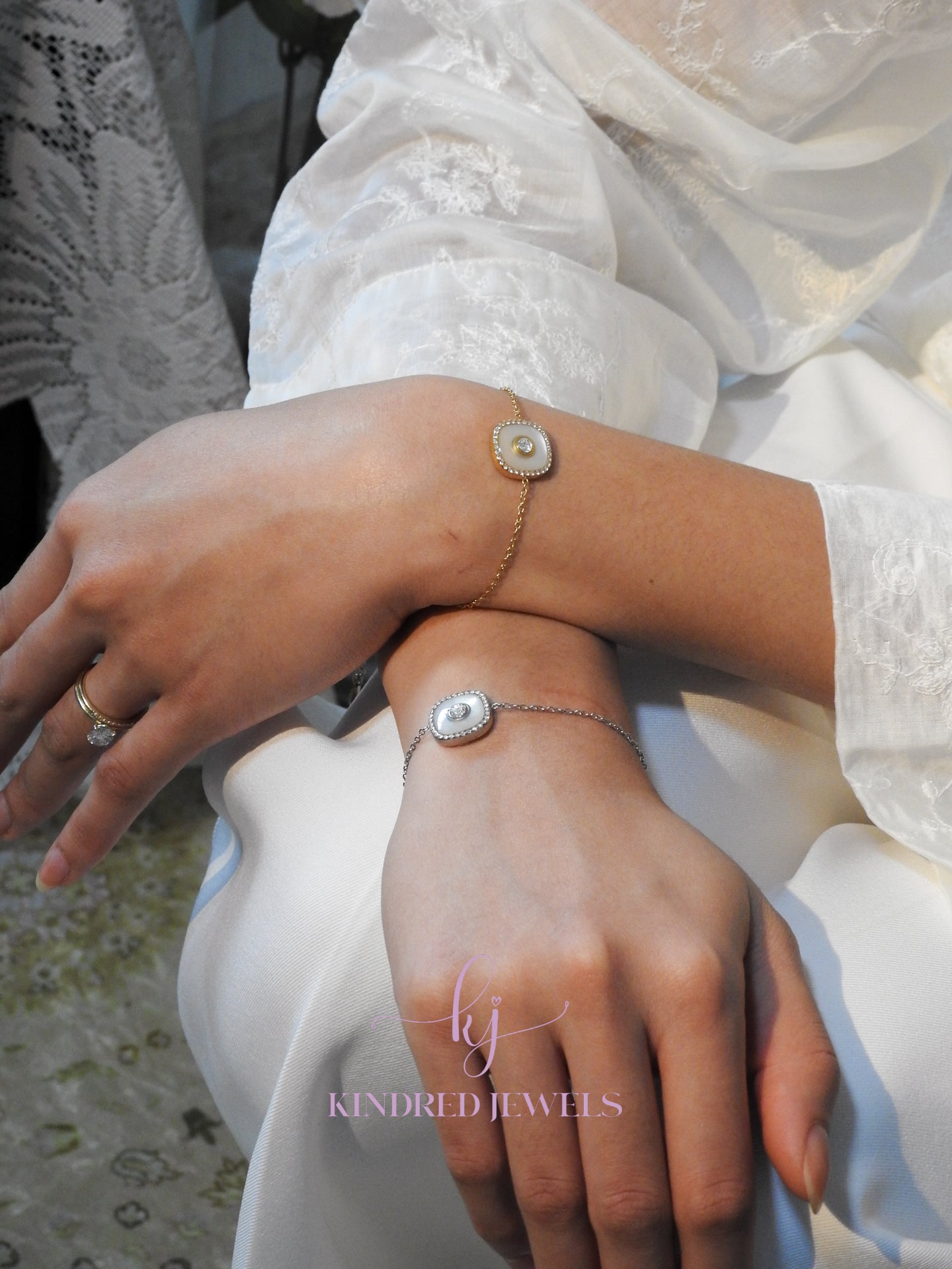 Close-up of hands wearing Kindred Jewels bracelets on a white fabric background.