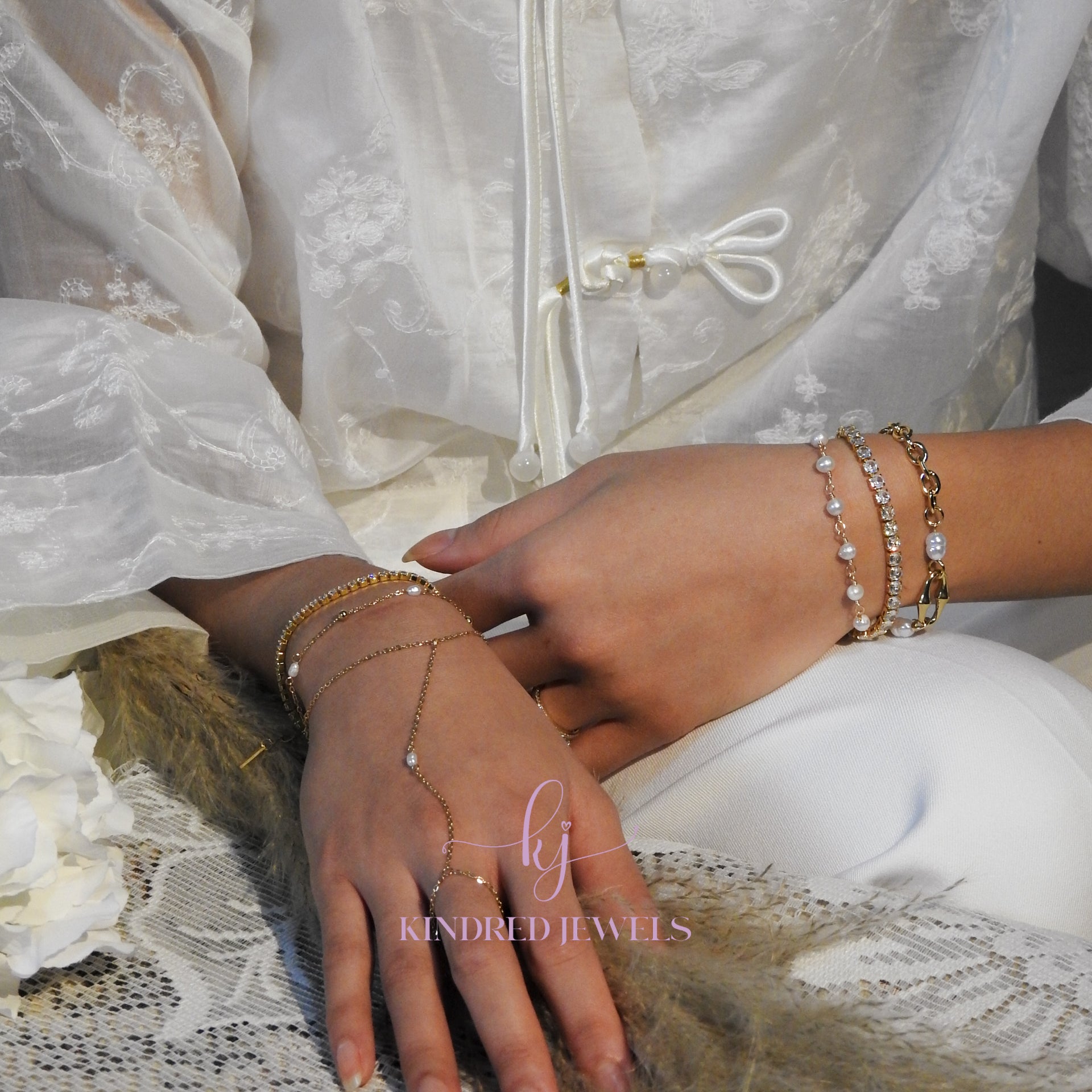 Close-up of hands wearing multiple bracelets with a brand name 'Kindred Jewels' in the corner.