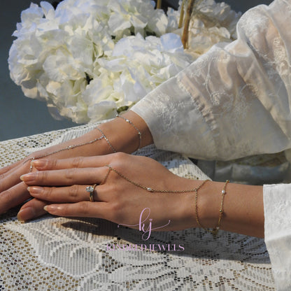 Close-up of hands wearing gold jewelry with a bouquet of white flowers in the background.