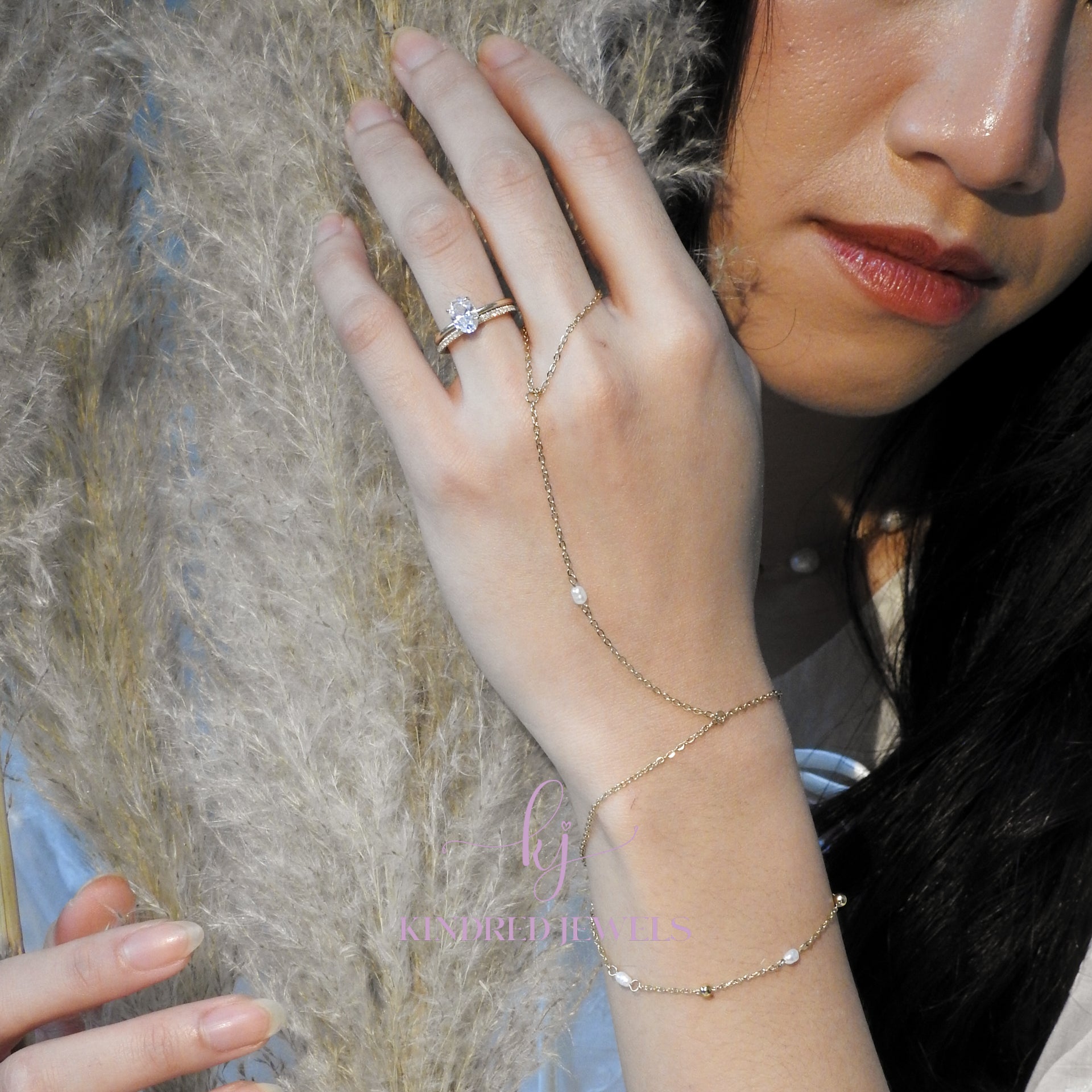 Close-up of a hand wearing a gold ring and bracelet, holding a dried plant.