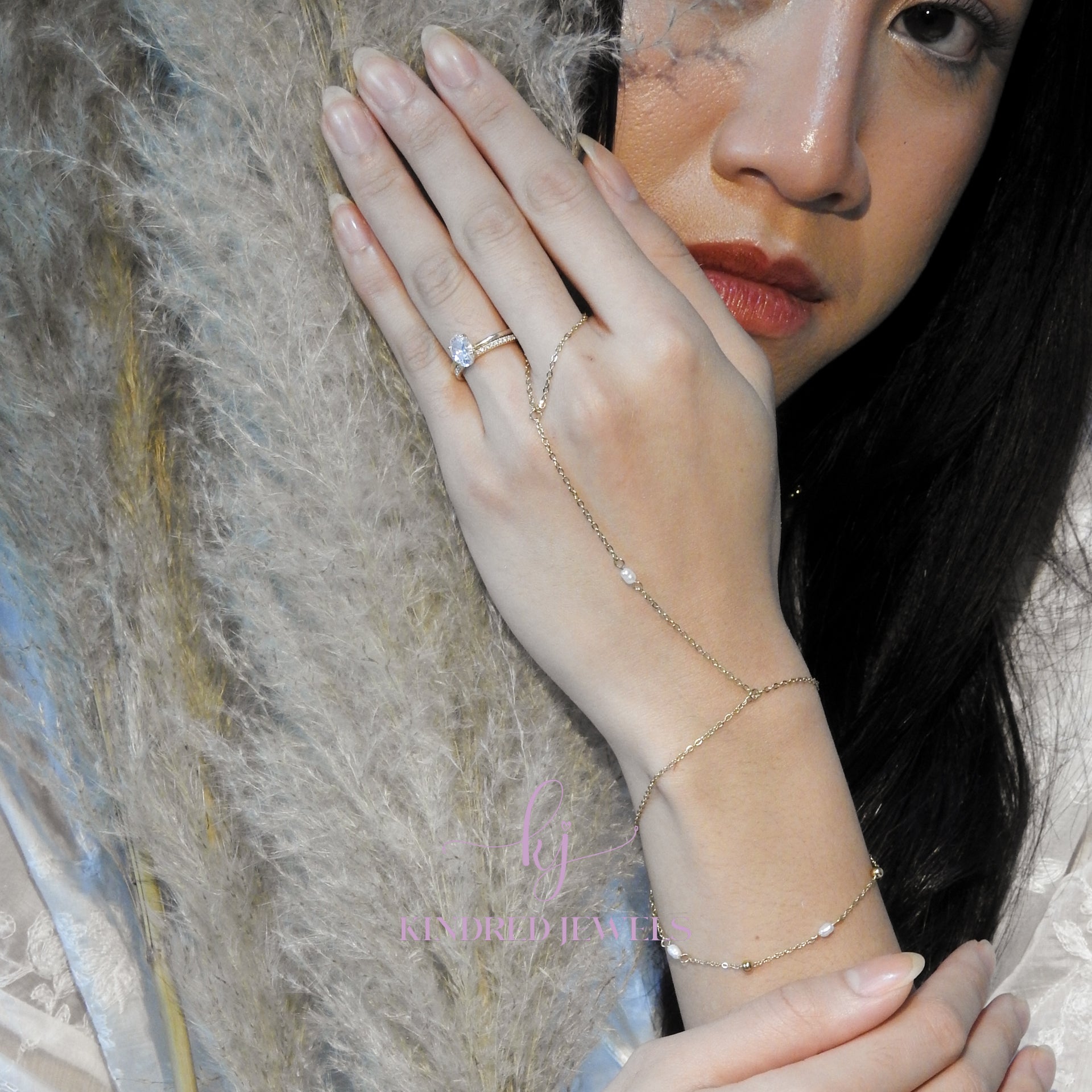 Close-up of a person's hand wearing a ring and bracelet with a neutral background