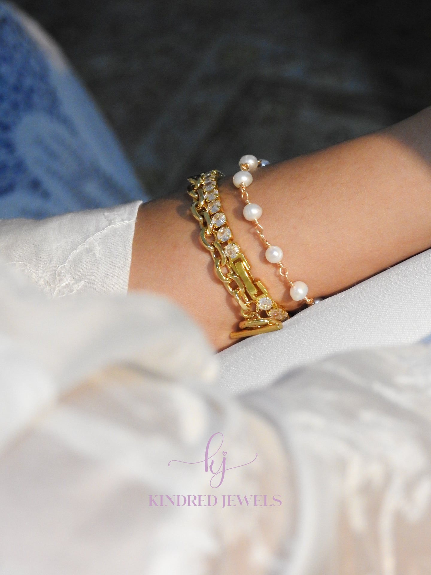 Gold chain and pearl bracelet on a wrist with 'Kindred Jewels' branding.