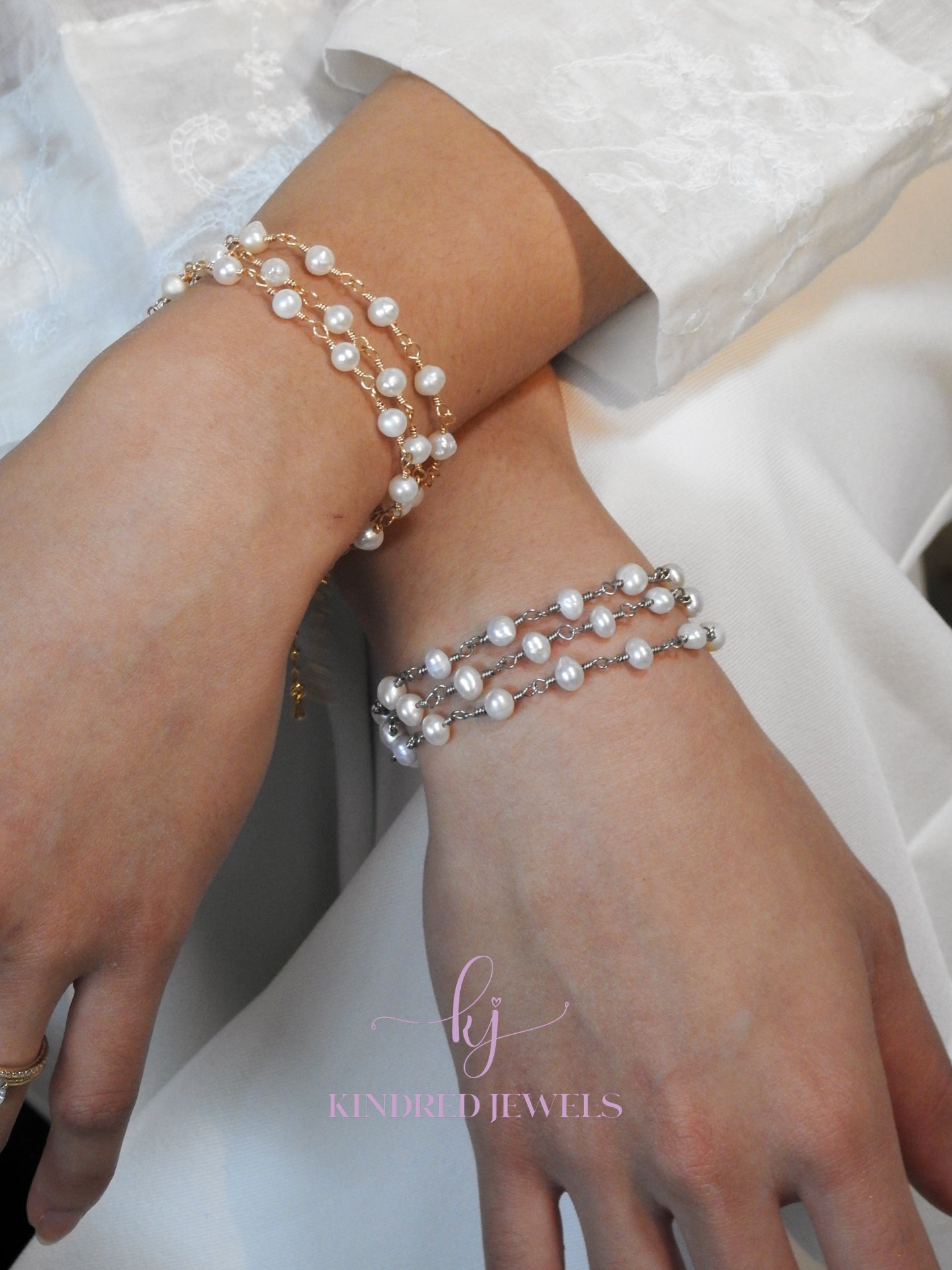 Two wrists wearing pearl bracelets with a visible brand logo.