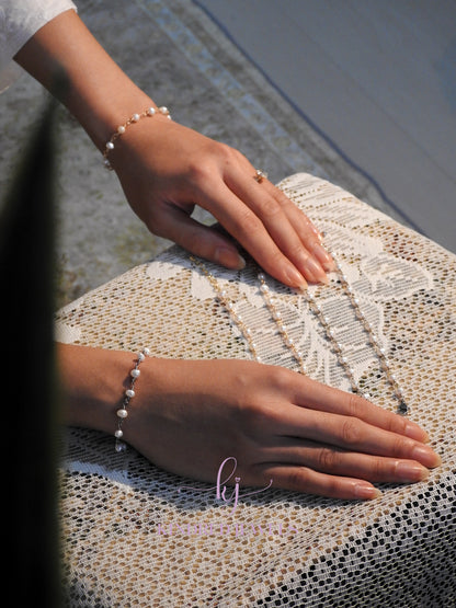 Close-up of two hands wearing pearl bracelets on a textured surface.